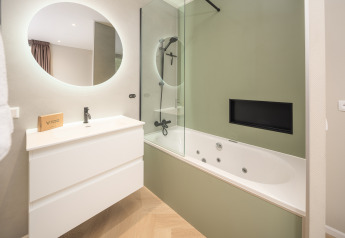 Baño moderno con espejo redondo, lavabo blanco y bañera de hidromasaje en Rosendael Comfort, Veluwepark de Bosgraaf, Países Bajos.
