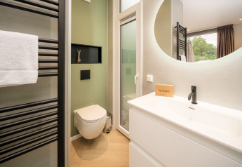 Modern bathroom in Rosendael Comfort lodge with green accent wall, mirror, and shower at Veluwepark de Bosgraaf.
