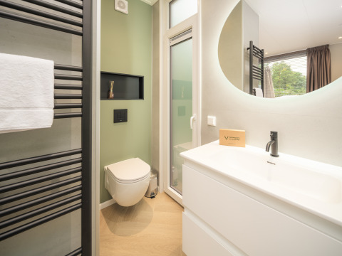Baño moderno en la cabaña Rosendael Comfort con pared verde, espejo y ducha en Veluwepark de Bosgraaf.