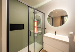 Bagno moderno con doccia in vetro, specchio rotondo e lavabo al Rosendael Comfort presso Veluwepark de Bosgraaf, Paesi Bassi.