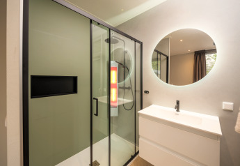 Modern bathroom with glass shower, round mirror, and sink at Rosendael Comfort lodge in Veluwepark de Bosgraaf, Netherlands.