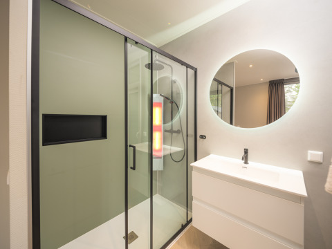 Baño moderno con ducha de vidrio, espejo redondo y lavabo en Rosendael Comfort en Veluwepark de Bosgraaf, Países Bajos.
