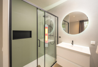 Moderne badkamer met glazen douche, ronde spiegel en wastafel in Rosendael Comfort aan Veluwepark de Bosgraaf, Nederland.