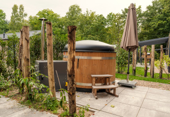 Außenansicht der Rosendael Comfort Lodge mit Holz-Hot-Tub und Sonnenschirm im Veluwepark de Bosgraaf.