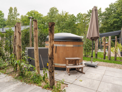 Außenansicht der Rosendael Comfort Lodge mit Holz-Hot-Tub und Sonnenschirm im Veluwepark de Bosgraaf.