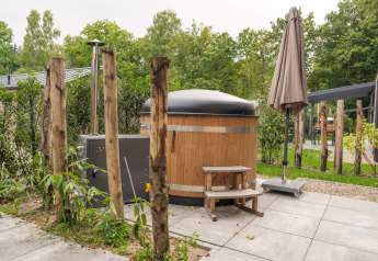 Udendørs billede af Rosendael Comfort-lodge med træ-hot-tub og parasol i Veluwepark de Bosgraaf.