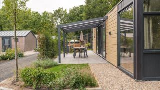 Moderne lodge med træfacade, overdækket terrasse og udendørs spisebord på Veluwepark de Bosgraaf i Holland.