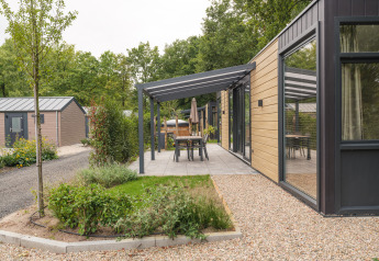 Moderne lodge med træfacade, overdækket terrasse og udendørs spisebord på Veluwepark de Bosgraaf i Holland.