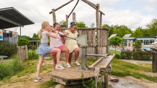 Drei Kinder spielen lachend an einer Wasserpumpe im Freizeitpark Vakantiepark Ackersate in Gelderland.