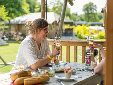 Due donne si godono vino e cibo sulla terrazza di una tenda safari al Vakantiepark Ackersate, Paesi Bassi.