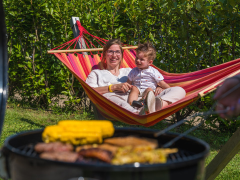 Mother and child relaxing in a hammock next to a barbecue at Villatent Nomad in Vakantiepark Ackersate.