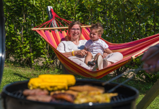 Moeder en kind ontspannen in een hangmat naast de barbecue bij Villatent Nomad op Vakantiepark Ackersate.