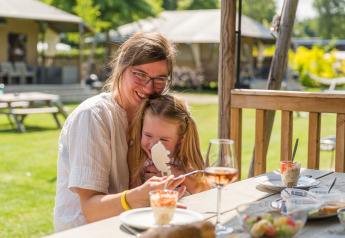 A mother and daughter enjoy dessert together outdoors at Villatent Nomad at Vakantiepark Ackersate, Netherlands.