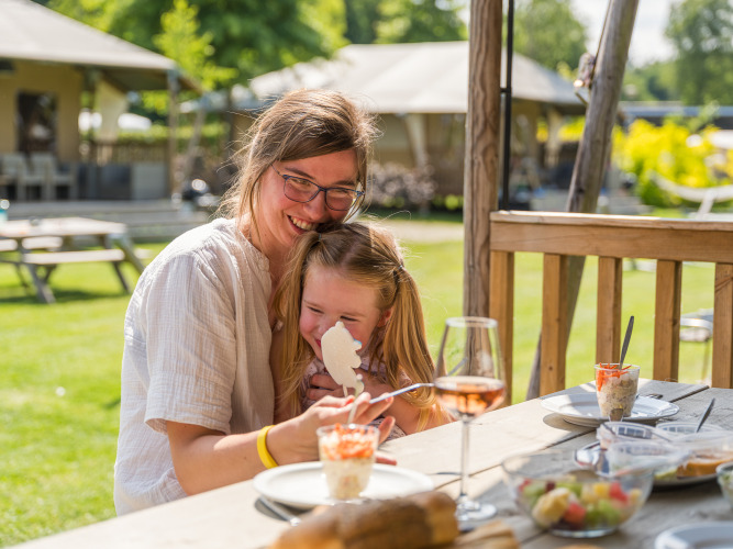 Mutter und Tochter genießen gemeinsam ein Dessert draußen bei Villatent Nomad im Vakantiepark Ackersate, Holland.