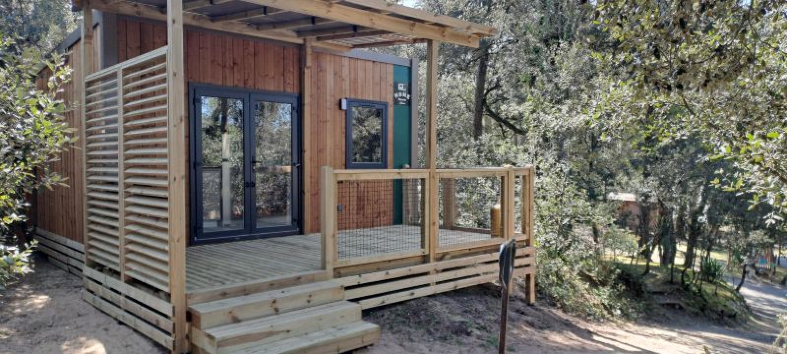 Standaard Mobilhome 23m2 met houten terras, moderne uitstraling, omgeven door bomen in de natuur.