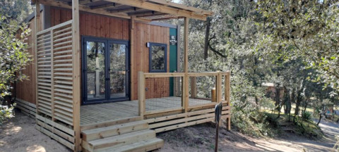 Mobilhome Standaard 23m2 con terrazza in legno, design moderno, immersa tra alberi e natura.