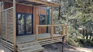 Standaard Mobilhome 23m2 met houten terras en moderne look, omgeven door bomen in een groene omgeving.