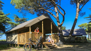 Familie genießt die Sonne vor einem komfortablen Safarizelt bei Flower Camping Monplaisir in Frankreich.
