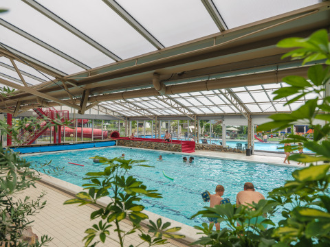Overdekt zwembad met glazen dak en rode glijbaan bij Vakantiepark Ackersate, Gelderland, Nederland.
