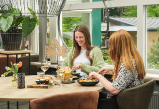 Dos mujeres disfrutan de una comida juntas en un espacio luminoso y moderno en Vakantiepark Ackersate, Gelderland.