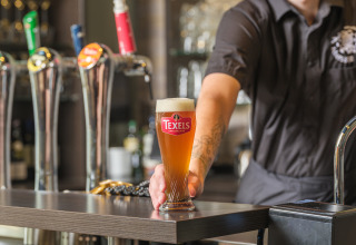 En bartender serverer et glas Texels øl ved en bar på Vakantiepark Ackersate i Gelderland, Holland.