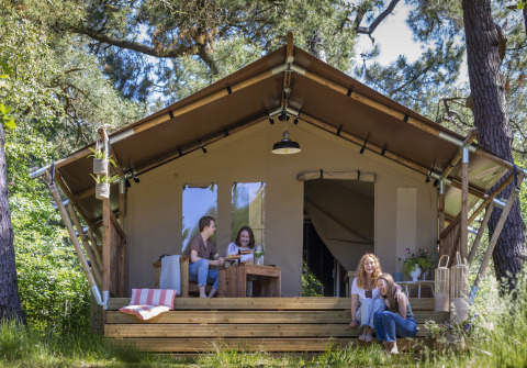 Cuatro mujeres se relajan y disfrutan frente a una tienda safari rodeada de árboles y naturaleza.