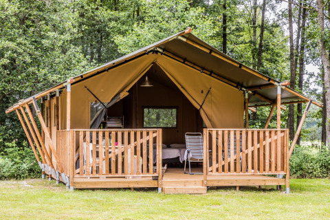 Safaritent met houten terras en stoelen, midden in het groen bos, perfect voor een ontspannen glamping.