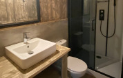 Bagno moderno di una sistemazione glamping con lavabo, doccia in vetro, WC e arredi in legno.