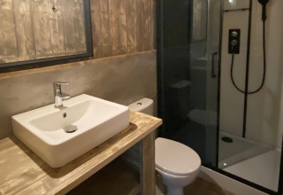 Bagno moderno di una sistemazione glamping con lavabo, doccia in vetro, WC e arredi in legno.