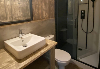 Moderne badkamer bij glamping met wastafel, toilet, glazen douche en rustieke houten wanden.
