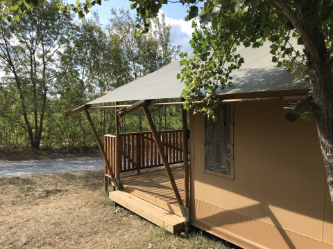 Safari-Zelt mit Holzveranda auf Camping Saint Amand in Frankreich, umgeben von grünen Bäumen.