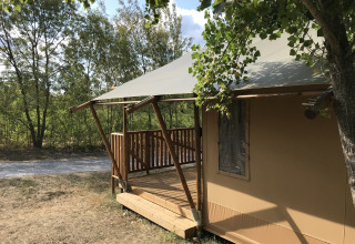 Tienda safari con porche de madera en Camping Saint Amand, Francia, rodeada de árboles y naturaleza.