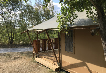 Safaritent met houten veranda op Camping Saint Amand in Frankrijk, omringd door bomen en natuur.