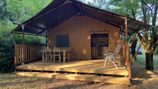 Safari-Zelt mit Sanitäranlagen, Holzmöbeln auf der Veranda, umgeben von grüner Natur und Bäumen.