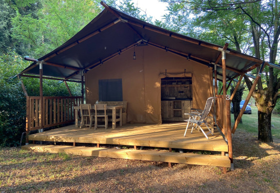Safari tent with sanitary facilities, wooden furniture on the porch, surrounded by green nature and trees.