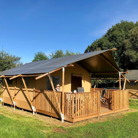 Tenda safari al Camping O2 in Francia con veranda in legno, sedie e tanto verde attorno sotto cielo sereno.