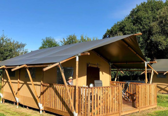 Tenda safari al Camping O2 in Francia con veranda in legno, sedie e tanto verde attorno sotto cielo sereno.