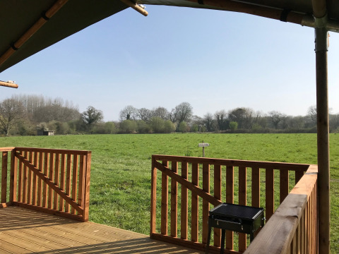 View from a safari tent deck at Camping O2 in France, overlooking a grassy field and distant trees.