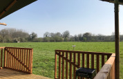 Vista desde la terraza de una tienda safari en Camping O2, Francia, con campo verde y árboles al fondo.