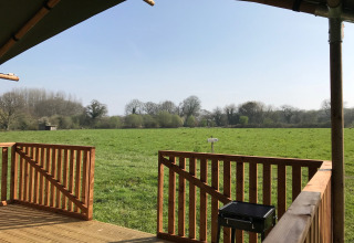 Blick von der Veranda eines Safarizeltes im Camping O2 in Frankreich auf eine grüne Wiese und Bäume.