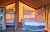 Interior of a safari tent with wooden floor, double bed with mosquito net and bunk bed divided by a canvas wall.