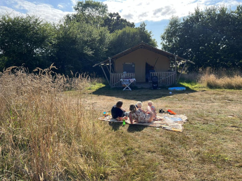 Family relaxing on a blanket in front of a safari tent at Camping O2 in France, enjoying the sunny weather.