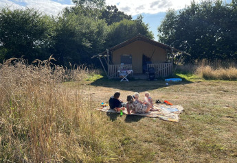 Famille profitant du soleil devant une tente safari au Camping O2 en France, entourée de verdure.