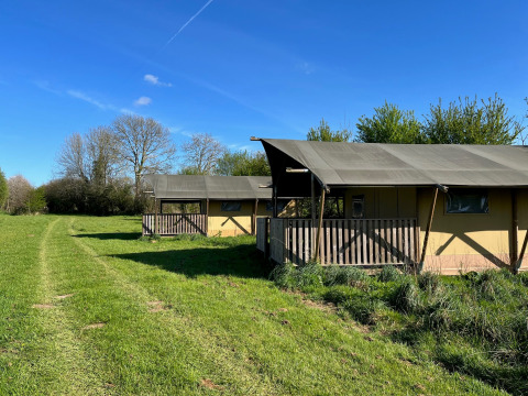 Safaritent bij Camping O2 in Frankrijk, te midden van grasveld en bomen onder een heldere blauwe lucht.