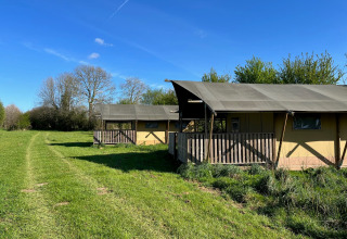 Tienda safari en Camping O2 en Francia, ubicada sobre césped con árboles y un cielo azul despejado.