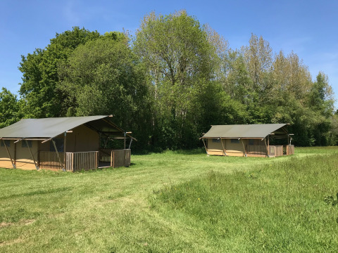 Tende safari al Camping O2 in Francia, situate su un prato verde con alberi sullo sfondo e cielo azzurro.