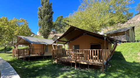 Safari-Zelt mit Sanitäranlagen, Holzveranda und grüner Umgebung unter blauem Himmel im Sommer.