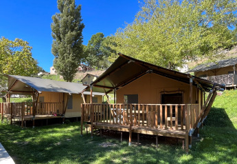 Safari-Zelt mit Sanitäranlagen, Holzveranda und grüner Umgebung unter blauem Himmel im Sommer.