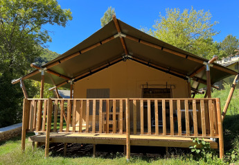 Safari tent with sanitary facilities at Camping l'Ardechois in France, nestled in greenery under a blue sky.