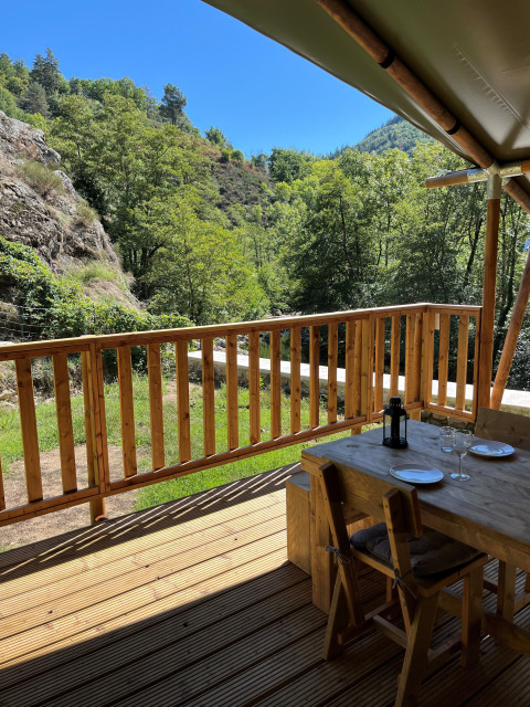 Vue d'une terrasse de tente safari avec mobilier en bois, collines verdoyantes et ciel bleu en France.
